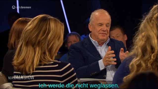 Vier Personen sitzen in einem Studio, eine davon spricht gestikulierend. Untertitel: "Ich werde die nicht weglassen."